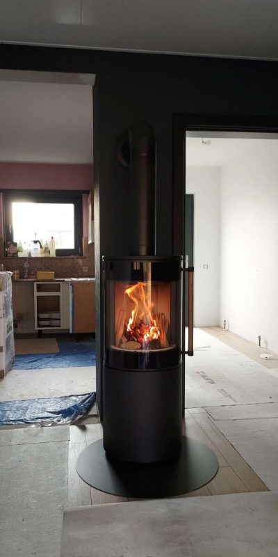 Poêle à bois cylindrique noir contre une cheminée maçonnée